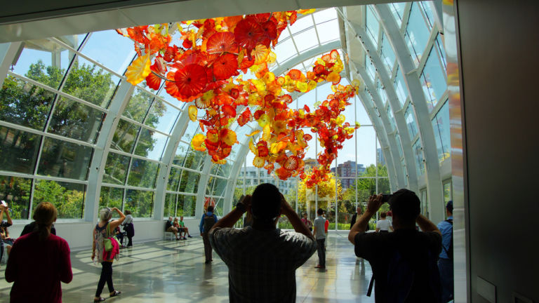 Tourists admire the Glass flowers in the conservatory sunlight of the Chihuly Garden and Glass Museum, Seattle, Washington