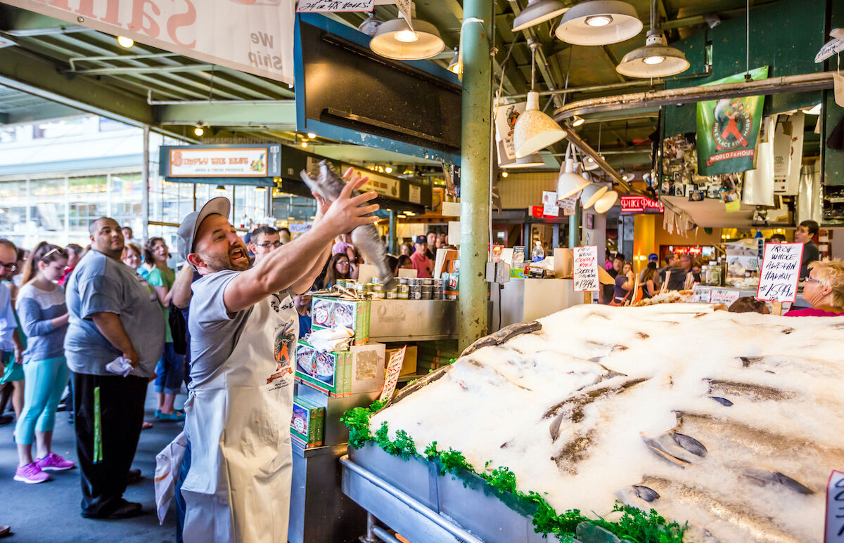 Customers at Pike Place Fish Company in Seattle, Washington. This market, opened in 1930, is known for their open air fish market style.