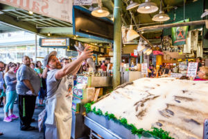 Customers at Pike Place Fish Company in Seattle, Washington. This market, opened in 1930, is known for their open air fish market style.