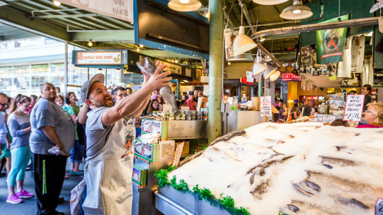 Customers at Pike Place Fish Company in Seattle, Washington. This market, opened in 1930, is known for their open air fish market style.