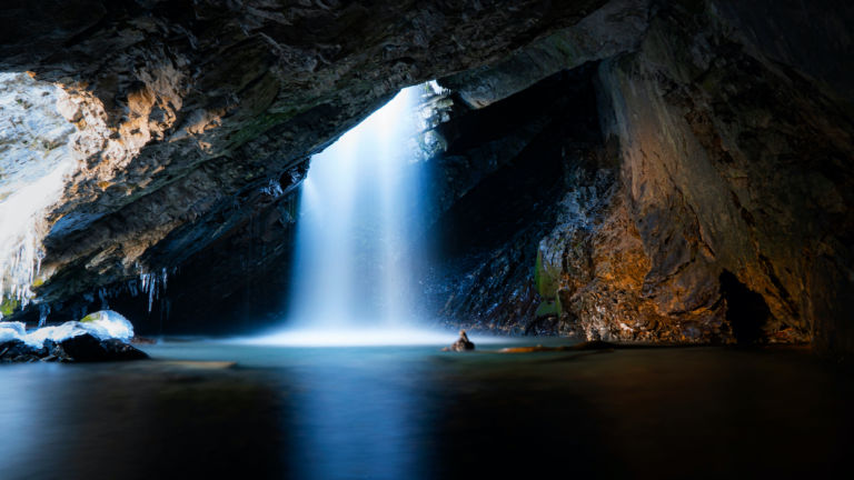 Beautiful shot of a stunning waterfall dropping down from a hole inside of a cave on a cold autumn day in Big Cottonwood Canyon located in Utah.