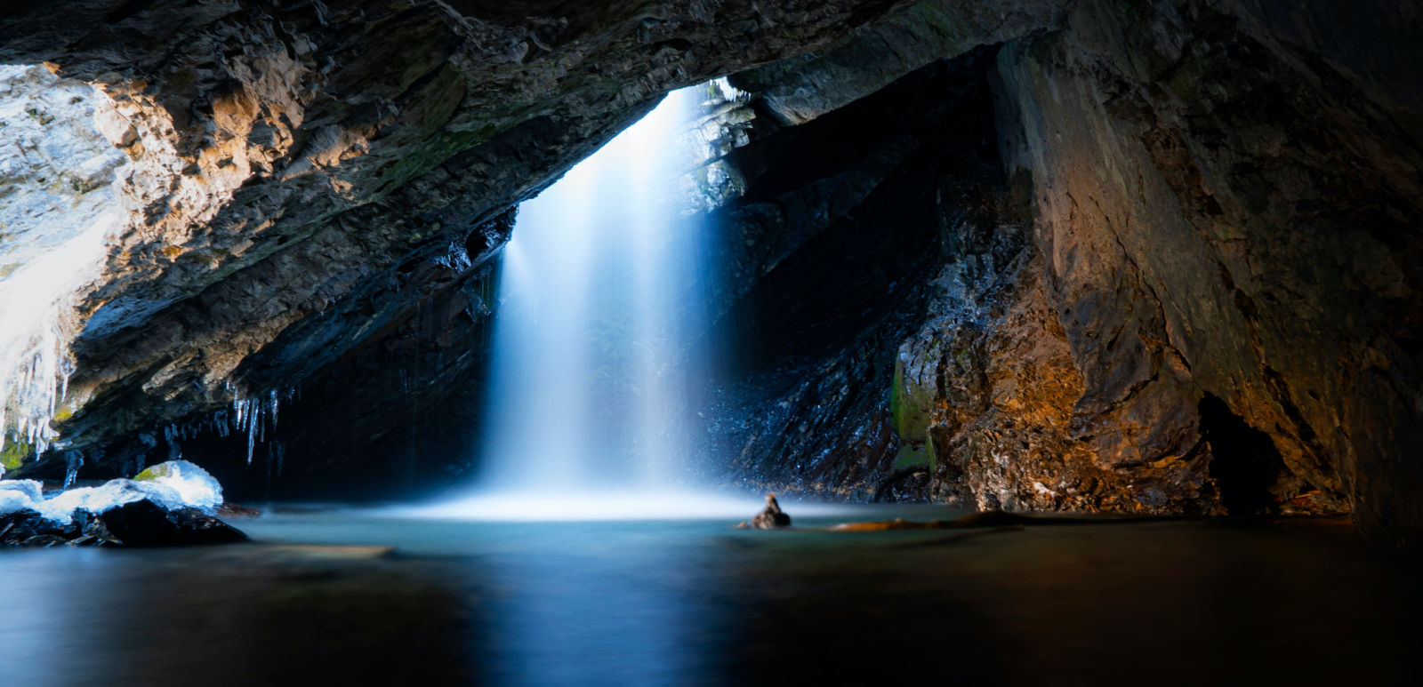 Beautiful shot of a stunning waterfall dropping down from a hole inside of a cave on a cold autumn day in Big Cottonwood Canyon located in Utah.