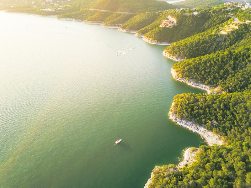 Greatest Summertime Lake Towns: Aerial trees and cliff rock wall, bluffs at Lake Travis, Austin, Texas. Photo via Shutterstock.