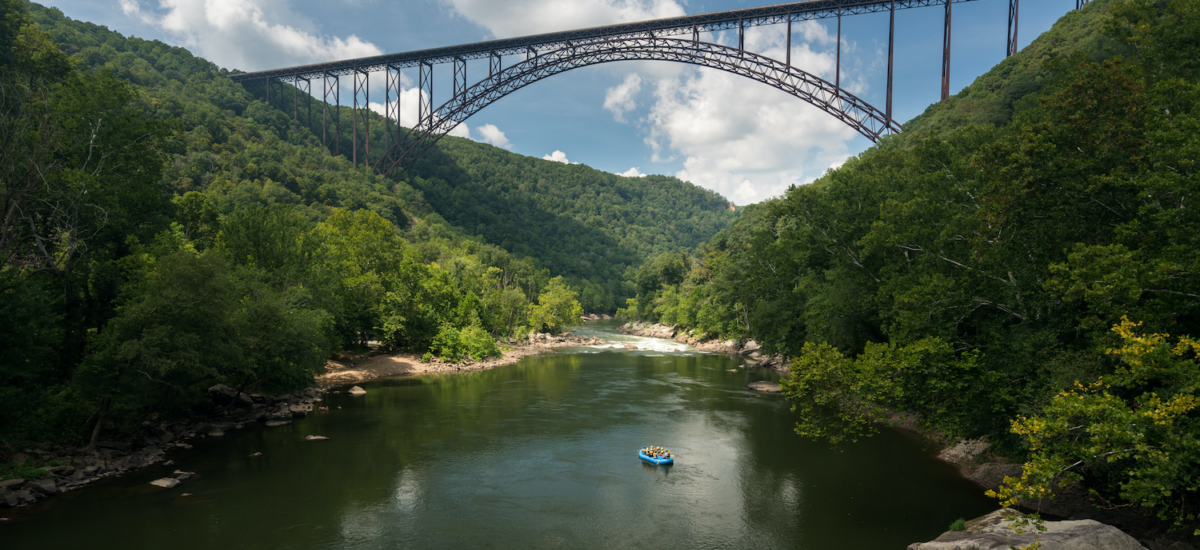 Rafters float towards the rapids under the high arched New River Gorge bridge in West Virginia