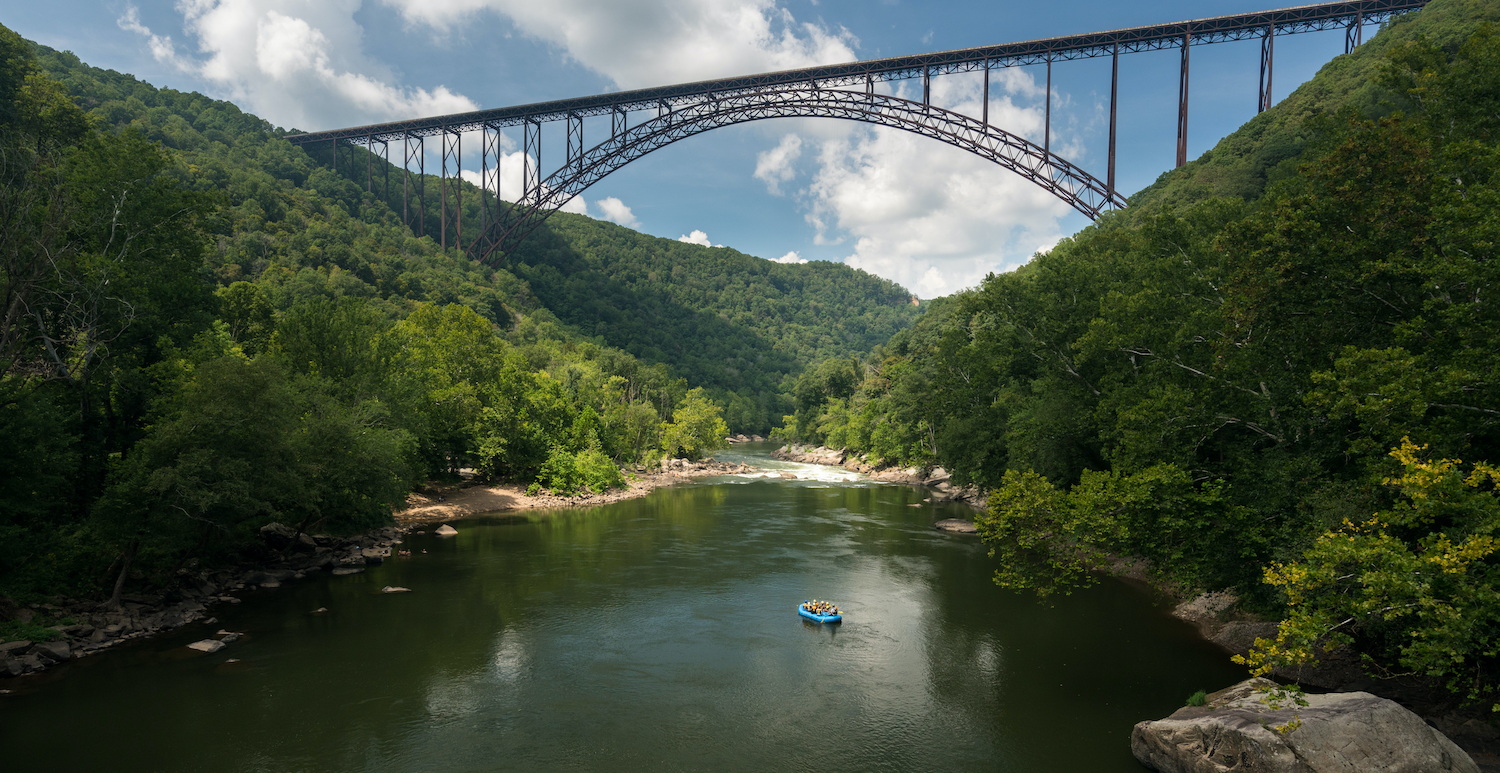 Rafters float towards the rapids under the high arched New River Gorge bridge in West Virginia