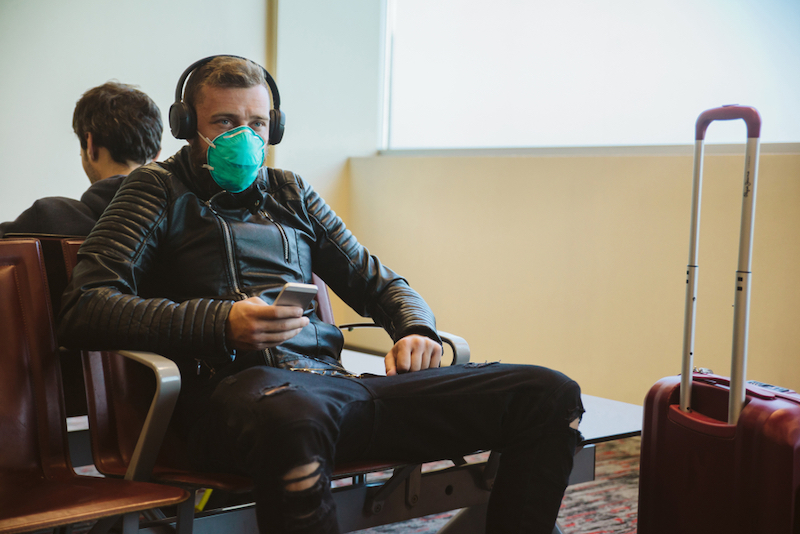 How to Take a Socially Distanced Summer Trip. Man wearing a mask protection at an airport. Photo by Shutterstock.