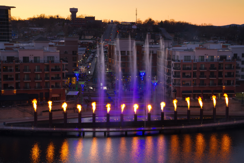 Skyline view of Branson, Missouri with the display showing at the landing waterfront park area.  The fountain has fire reflection into the water with tourist watching as they shop. Photo by Shutterstock.