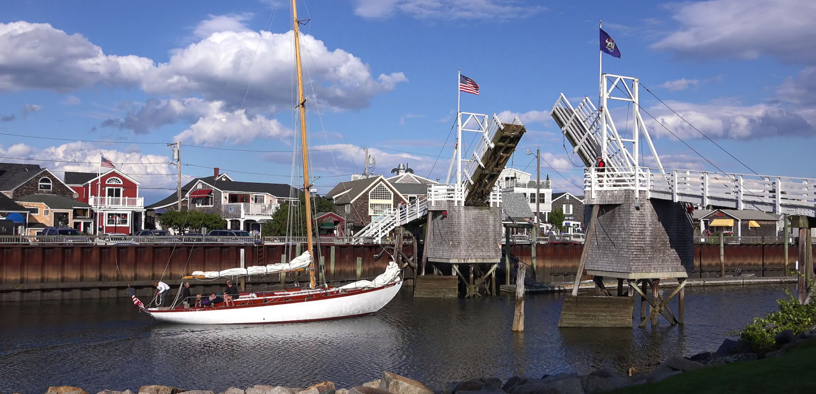 Sailboat heads out to sea under cross over walking draw bridge, scenic blue sky clouds, Perkins Cove Ogunquit, Maine USA - September 18, 2014