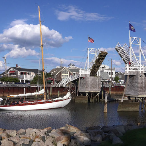 Sailboat heads out to sea under cross over walking draw bridge, scenic blue sky clouds, Perkins Cove Ogunquit, Maine USA - September 18, 2014