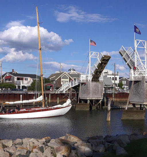 Sailboat heads out to sea under cross over walking draw bridge, scenic blue sky clouds, Perkins Cove Ogunquit, Maine USA - September 18, 2014