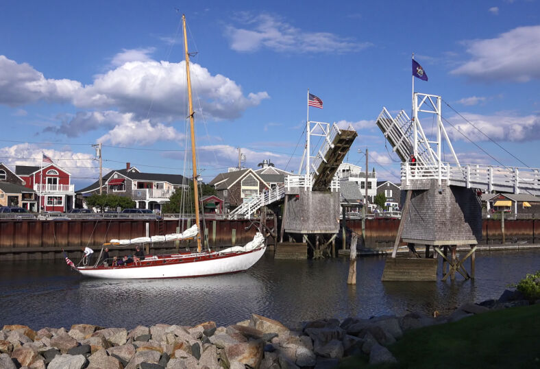 Sailboat heads out to sea under cross over walking draw bridge, scenic blue sky clouds, Perkins Cove Ogunquit, Maine USA - September 18, 2014