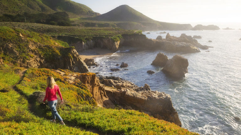 A female hiker walks down a trail in Big Sur, California.