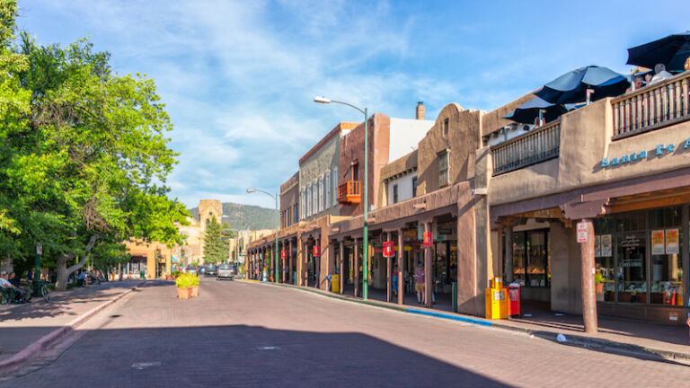 Santa Fe, New Mexico - June 14, 2019: Old town street in United States New Mexico city with adobe style architecture and church. Photo via Shutterstock.