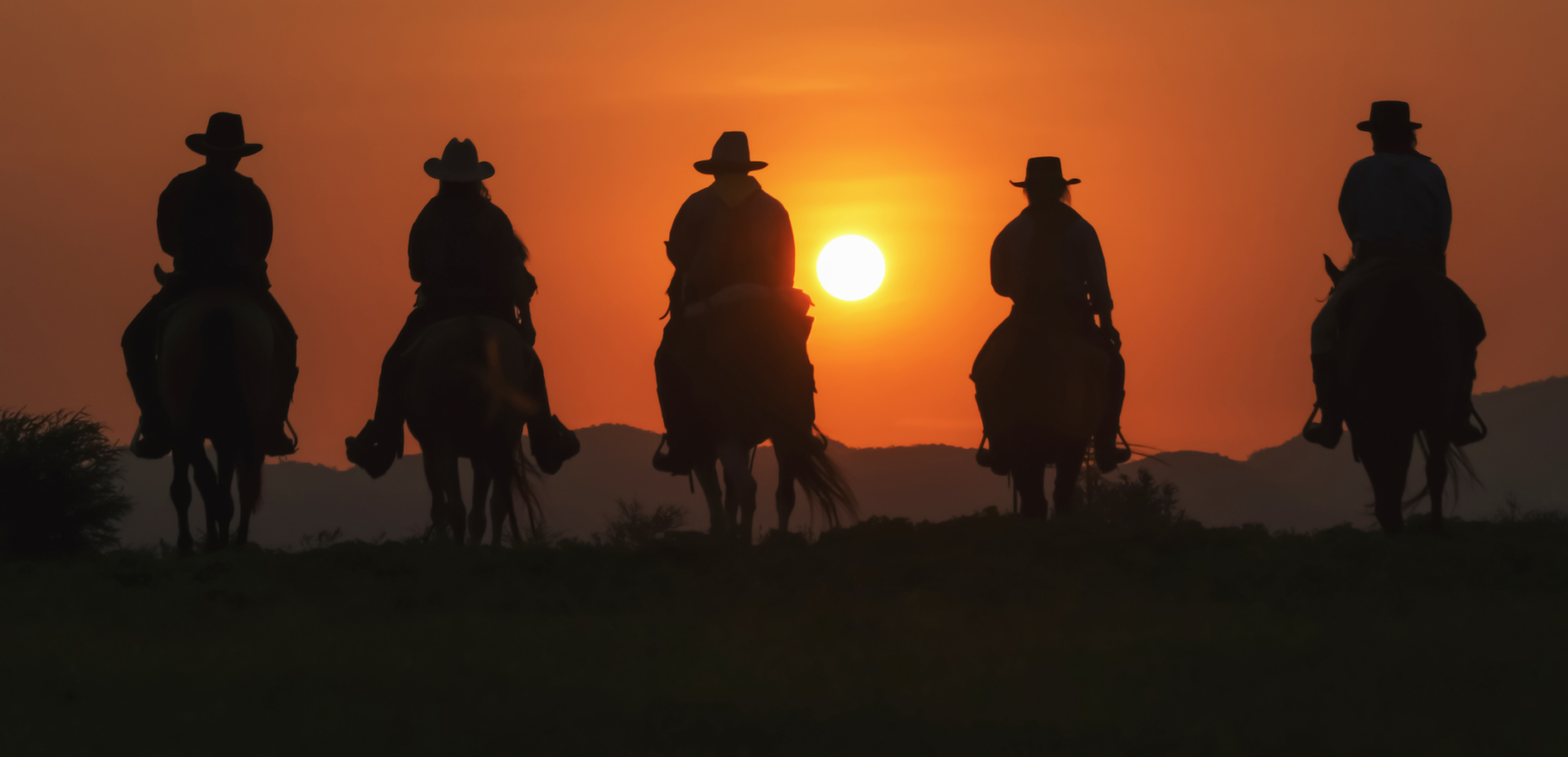 Vintage and silhouettes of a group of cowboys sitting on horseback at sunset.