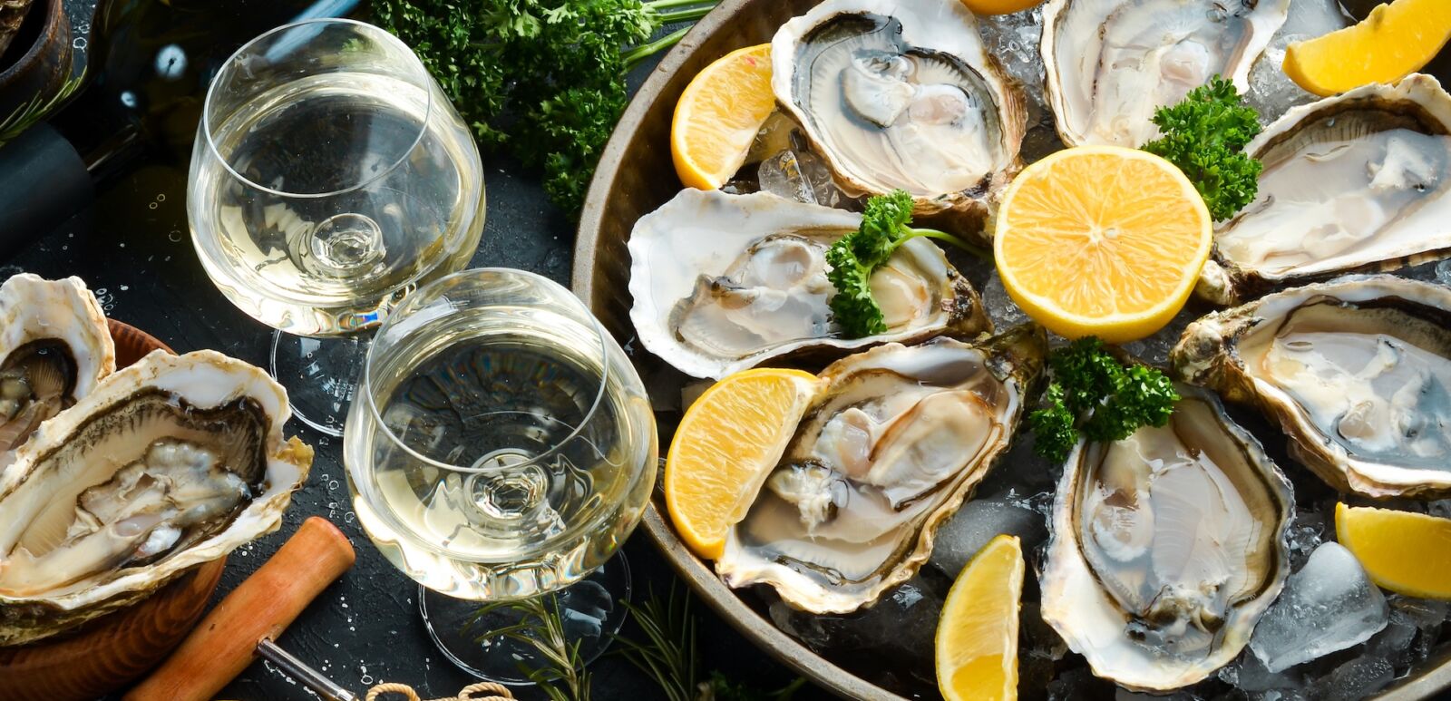 Bottle of aged wine and fresh oysters on a dark kitchen table. Seafood. Top view. Photo via Shutterstock.