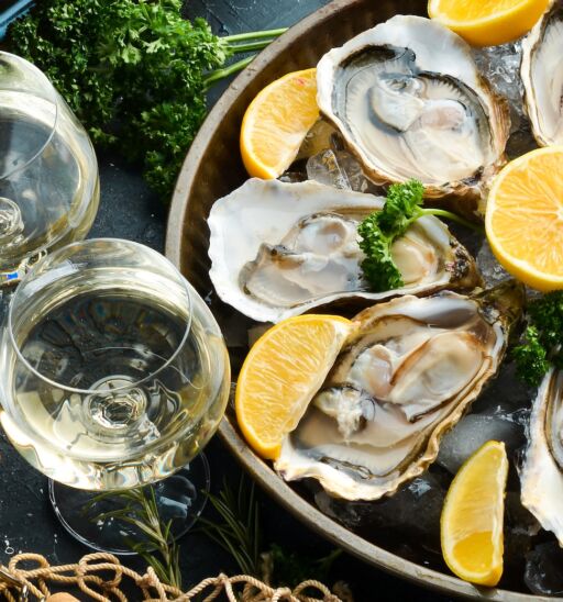 Bottle of aged wine and fresh oysters on a dark kitchen table. Seafood. Top view. Photo via Shutterstock.