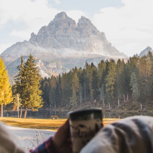 Woman enjoys cup of coffee out back of van while living the nomadic van life (vanlife) lifestyle in Europe on a cold autumn morning.